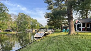 A grassy area with a dock and boats, a covered structure, and a building with an American flag.