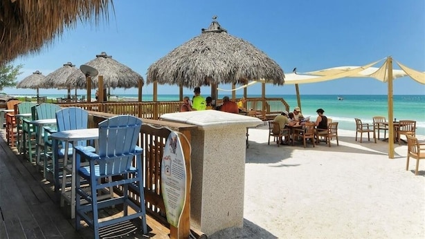 Un restaurante frente al mar con sombrillas de paja, mesas y sillas de madera.