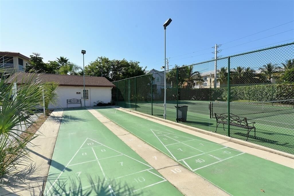 A green shuffleboard court with a fence, a trash bin, and a bench.