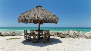 Una playa con una sombrilla de paja, sillas de madera y una mesa.