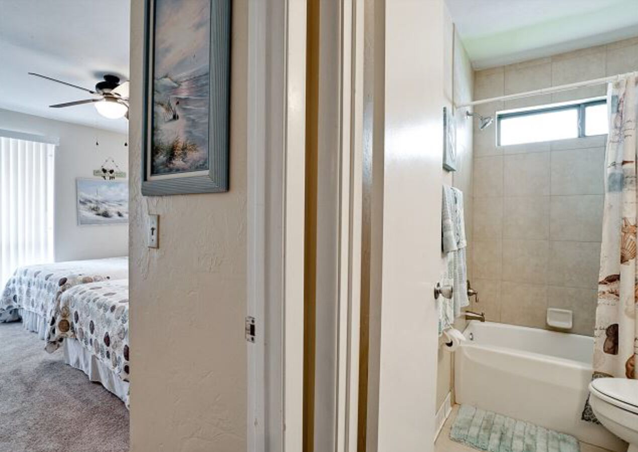 Une chambre avec deux lits, une salle de bain avec une baignoire et un ventilateur de plafond.