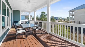 Une terrasse extérieure couverte, dotée d’une table et de chaises, de rampes blanches et offrant une vue sur les maisons voisines.