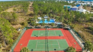 Vue aérienne d’un court de tennis entouré d’arbres et bordé d’une zone de piscine.