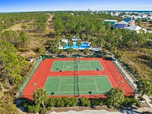 Vue aérienne d’un court de tennis entouré d’arbres et bordé d’une zone de piscine.