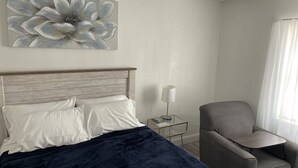 Une chambre d’hôtel avec un lit, une chaise, une table de chevet, une lampe et une grande œuvre d’art florale accrochée au mur.