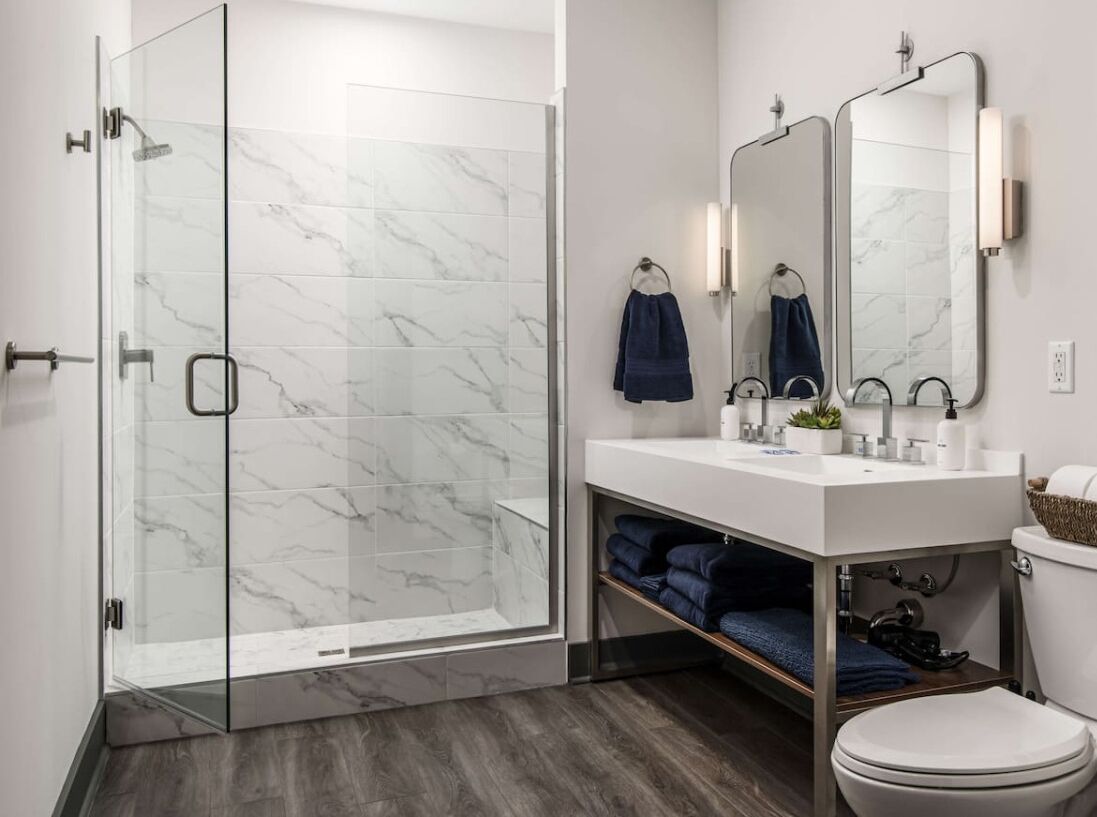 A modern bathroom with a glass-enclosed shower, a white sink with a mirror, and a toilet.