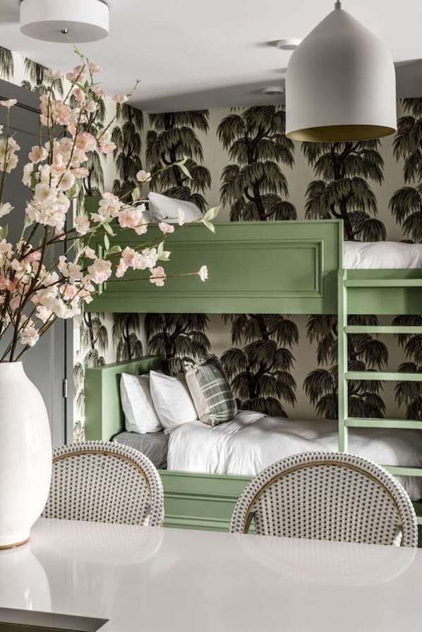 A bunk bed with a green headboard, white bedding, and a white vase with pink flowers.