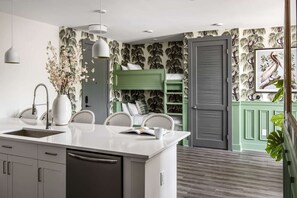 Una cocina moderna con encimera blanca, un lavamanos empotrado y una zona de comedor con sillas de mimbre.