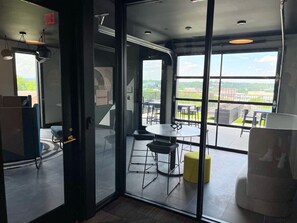 A modern interior with a glass partition, a round table with stools, and a view of the outdoors.