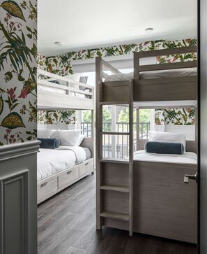 A room with a bunk bed, a desk, and a window with a view of greenery.