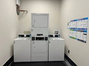 A laundry facility with three washers and dryers, a water heater, and instructional posters on laundry best practices.