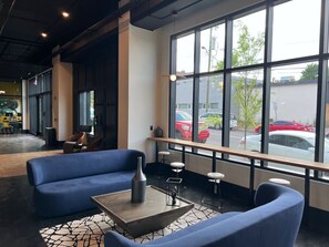 A modern interior with blue seating, a coffee table, and large windows offering a view of parked cars and trees.