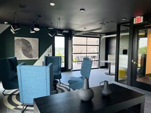 A modern lobby with blue chairs, a black table with vases, and a large window with a view of the outdoors.