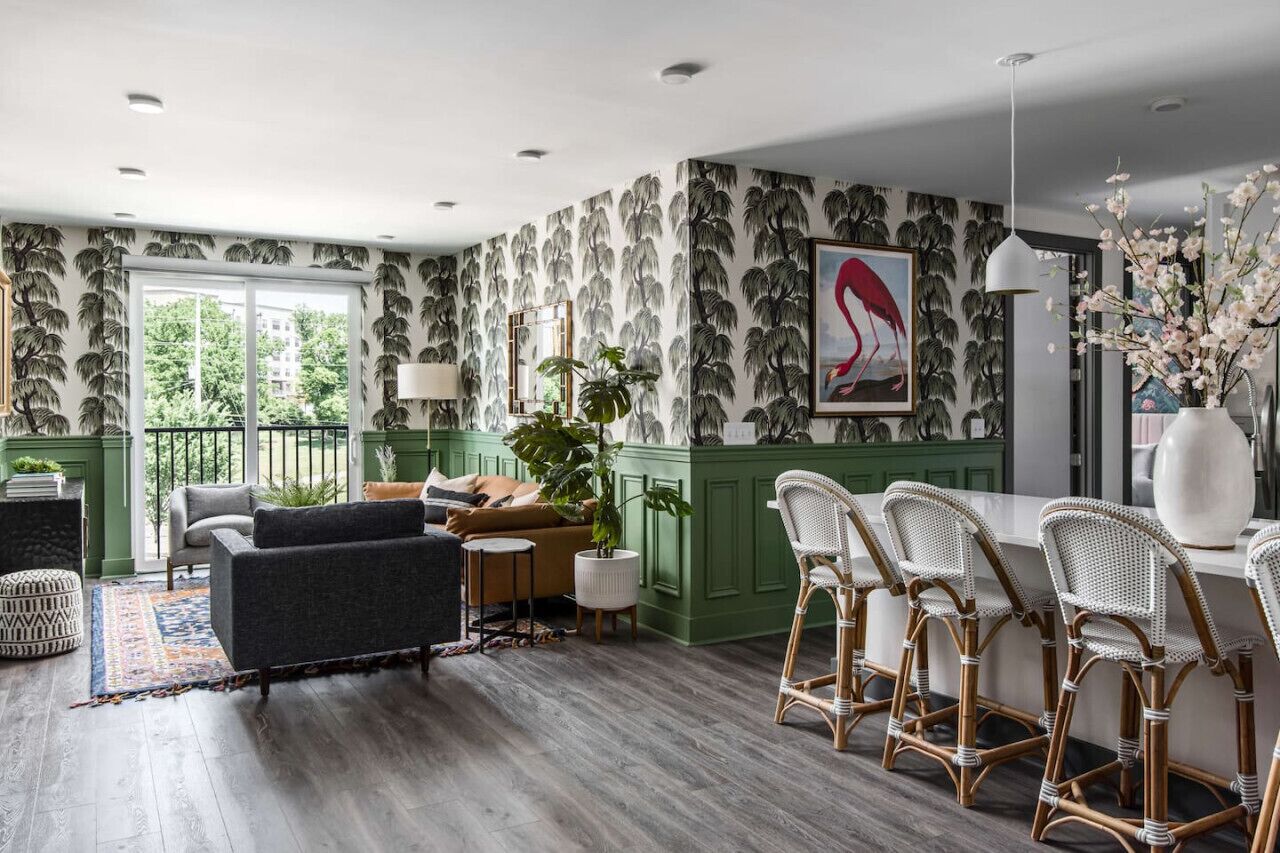 Una sala de estar moderna con una pared verde de acento, un ventanal grande y una zona de comedor con sillas de mimbre.