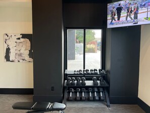A gym with exercise equipment, a television displaying news, and a large window with a view of the outside.