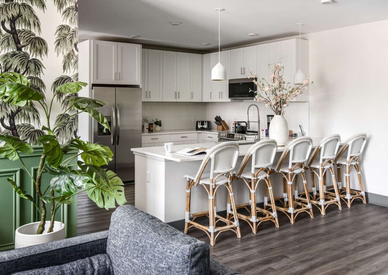 Una cocina moderna con armarios blancos, una isla central con taburetes de bar, un refrigerador y un microondas.
