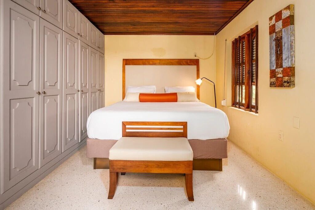 A bedroom with a large bed, a wooden bench, and a wardrobe.