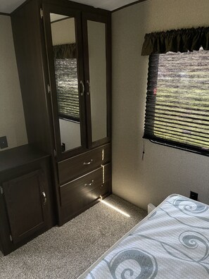 Quarto com cama, guarda-roupa, espelho e janela com persianas.