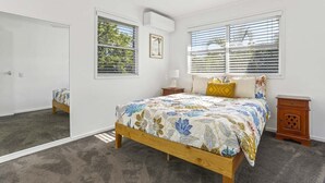 A bedroom with a bed, two bedside tables, a ceiling fan, and two windows with blinds. - Peaceful Family Villa in Sunrise Beach (Sunrise Beach)