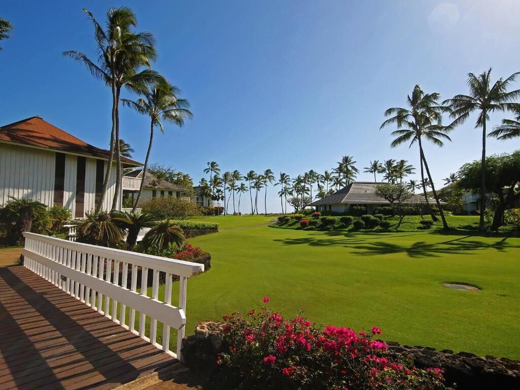 A well-maintained golf course with a wooden deck and a white railing, surrounded by palm trees and a clear blue sky.