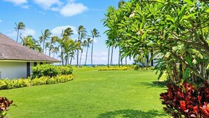 A well-maintained lawn with a building on the left, palm trees, and a clear view of the ocean. - Luxury Ground Floor Condo Just 50 Yards From The Beach! (Koloa)