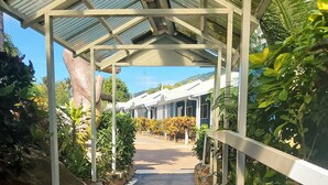A covered walkway with a tiled floor, flanked by plants and a stone wall.