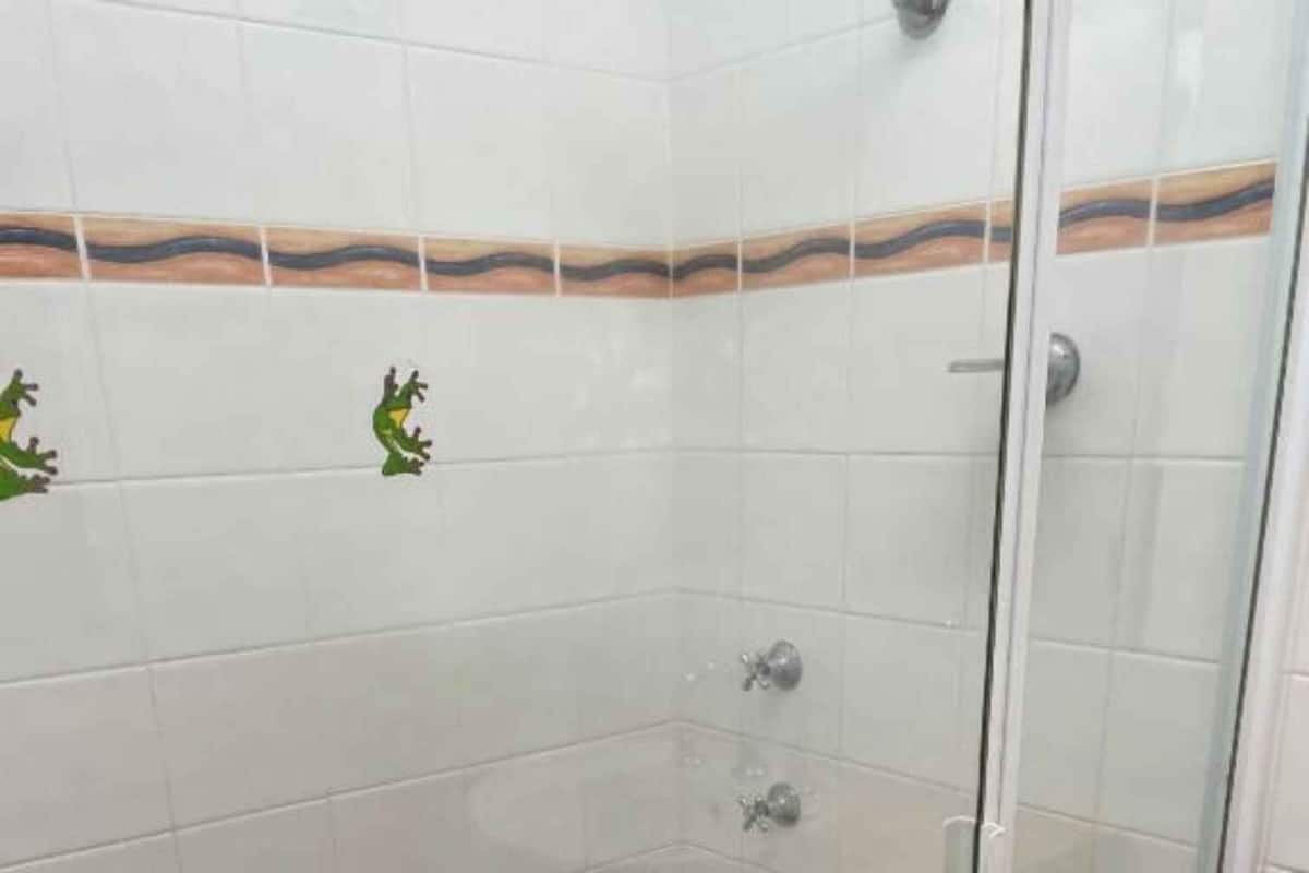 A small, enclosed shower area with white tiles and a brown floor.