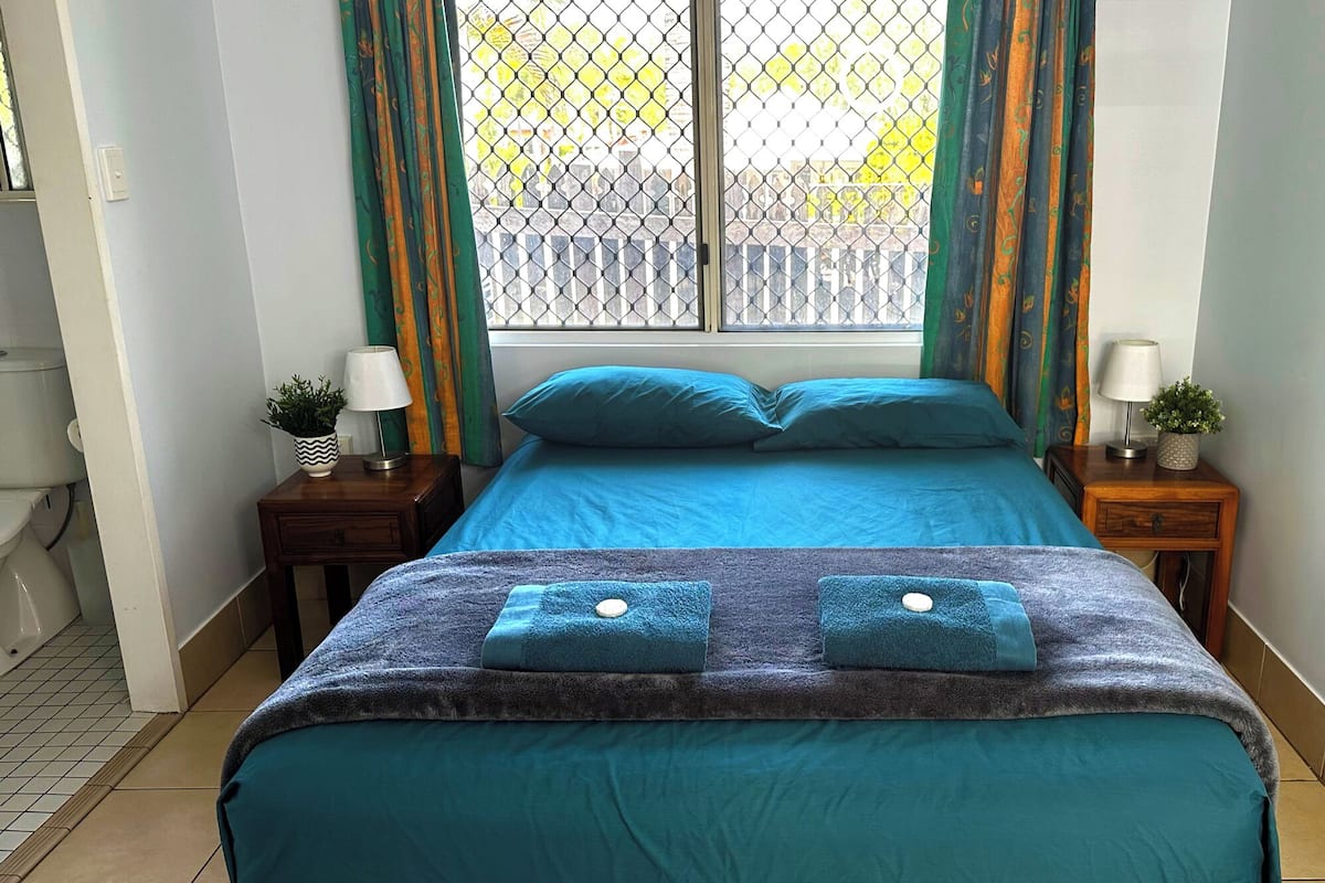 A bedroom with a bed, two nightstands, a window with curtains, and a view of the outside.