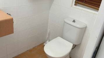 A small bathroom with a toilet, a towel rack with two towels, and a window with blinds.