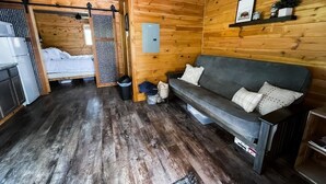 Tunnelmallinen mökin sisustus, jossa on puulattia, sohva, sänky ja pieni keittiöalue.