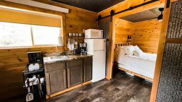 A compact log cabin with a kitchenette, a bed, and a sliding door.