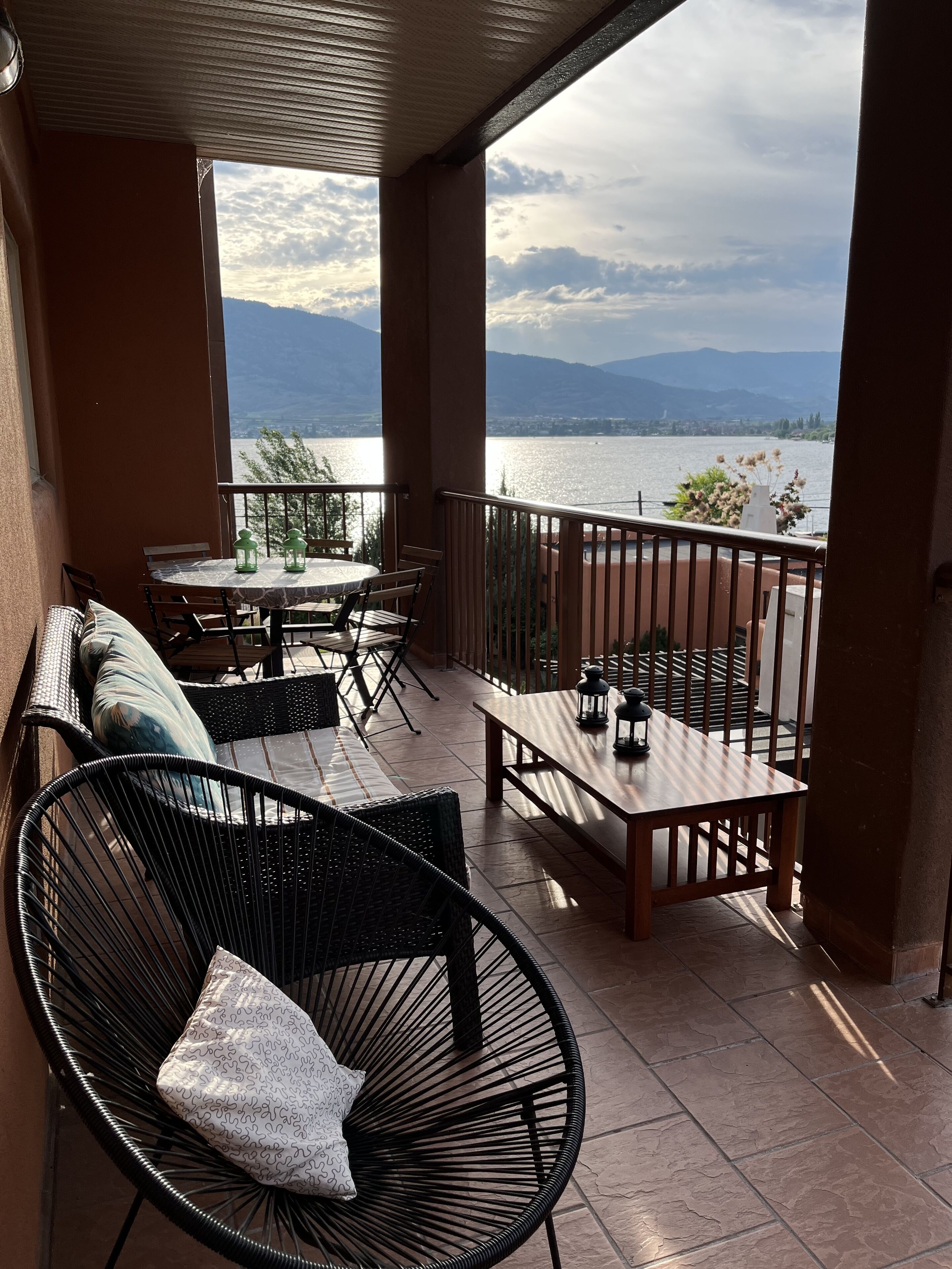 Un balcon avec une table et des chaises, donnant sur un lac et des montagnes.
