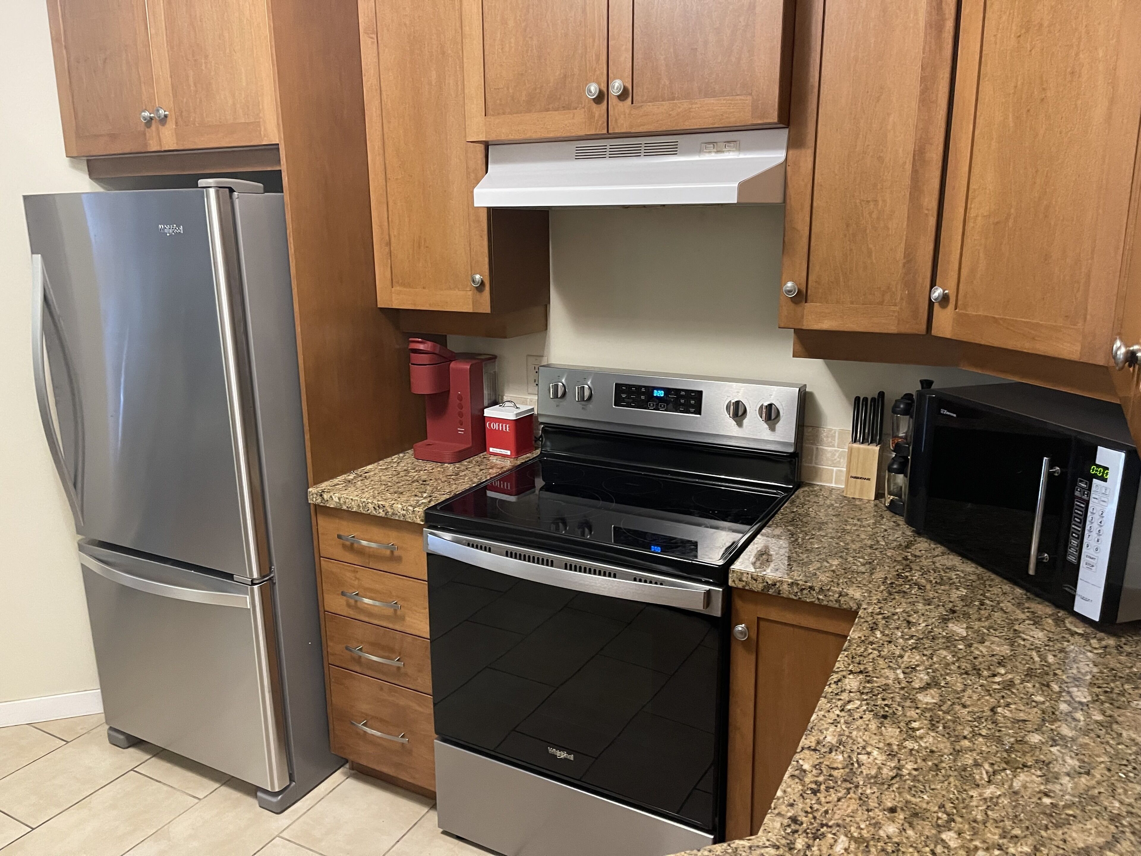 A kitchen with a stainless steel refrigerator, a black oven, a microwave, and wooden cabinets.