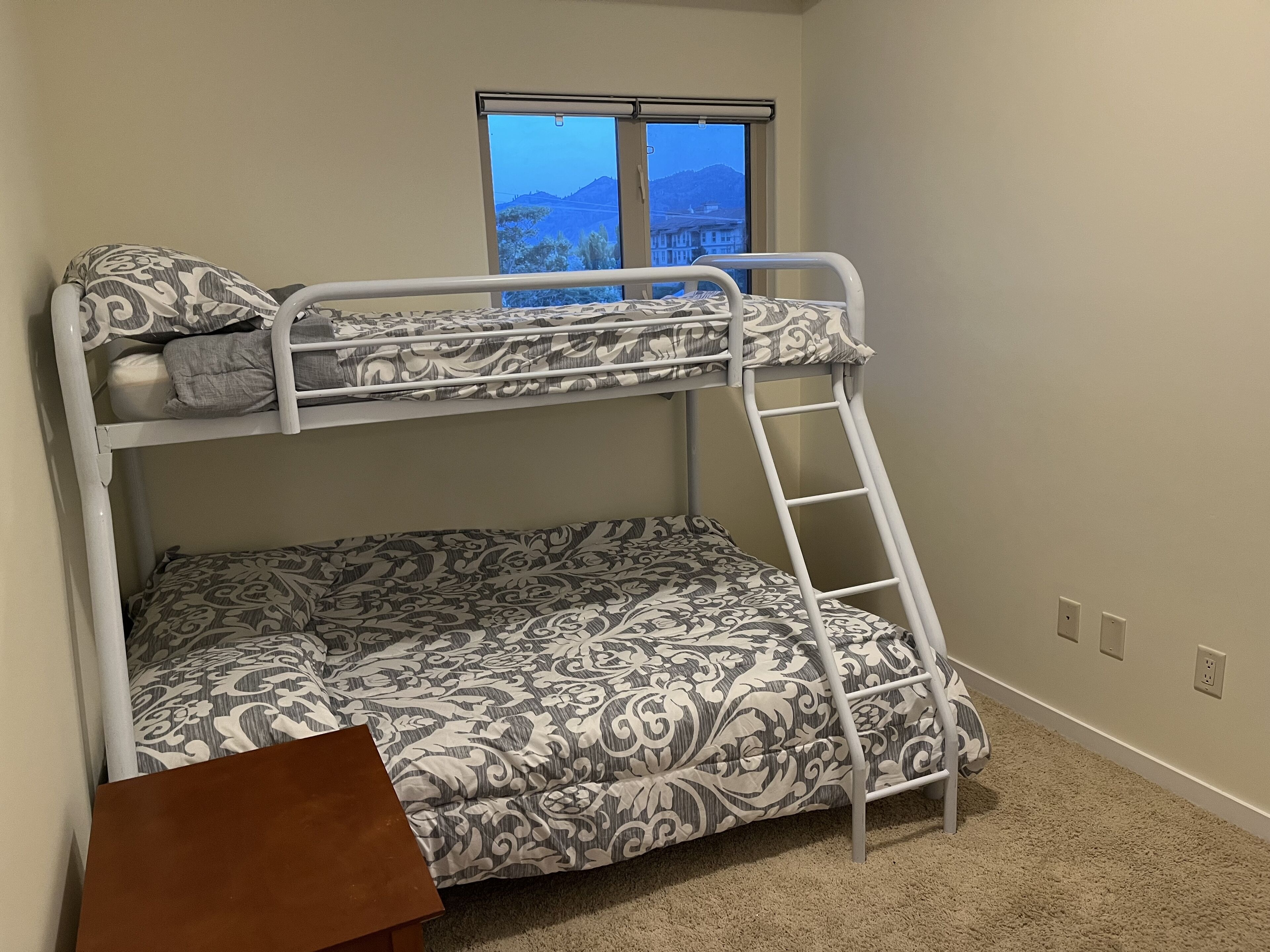 A bunk bed room with patterned bedding, a window with a view, and a small wooden table.
