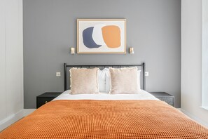 A modern bedroom with a bed, two nightstands, a framed abstract artwork, and a textured orange throw blanket.