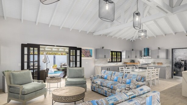 A spacious living room with a sofa, armchairs, and a round coffee table. A kitchen with modern appliances and a dining area with a table and chairs is visible through an open door. - 4BR4BA Private Pool,Sauna, Putt-Putt & Fire Place (Noord)