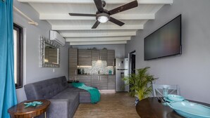 A modern living room with a grey sofa, a dining table with blue plates, a ceiling fan, and a kitchen area with grey cabinets. - 4BR4BA Private Pool,Sauna, Putt-Putt & Fire Place (Noord)