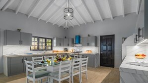 A modern kitchen with a large island, white cabinetry, and a dining area with white chairs. - 4BR4BA Private Pool,Sauna, Putt-Putt & Fire Place (Noord)