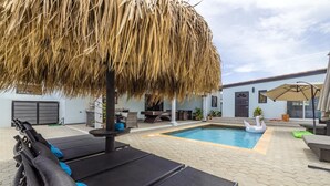 A pool area with a thatched umbrella, lounge chairs, and a swan float. - 4BR4BA Private Pool,Sauna, Putt-Putt & Fire Place (Noord)