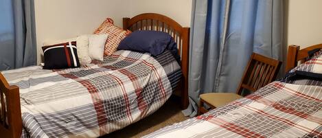 Een slaapkamer met twee eenpersoonsbedden, een houten hoofdbord, een klein tafeltje en lichtblauwe gordijnen.
