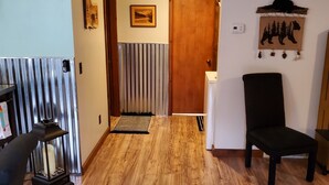 Un pasillo con suelo de madera, una silla negra, un radiador y una puerta con un cuadro encima.