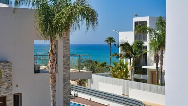 A modern building with a pool, palm trees, and a view of the ocean.