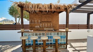 An outdoor bar area with a thatched roof, a wooden counter, and four stools.