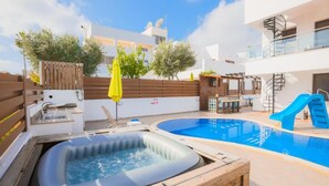 A swimming pool with a hot tub, a slide, and a wooden deck.