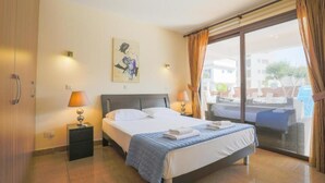 A hotel room with a bed, two bedside tables, a painting, and a view of the outside.