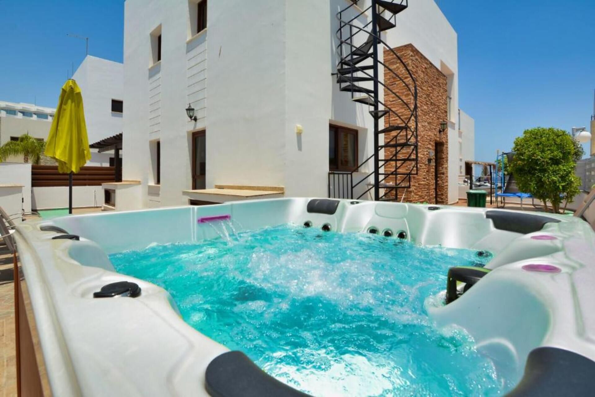 Un jacuzzi con piscina azul cristalina, rodeado por un edificio blanco de fachada de piedra y una escalera de caracol.