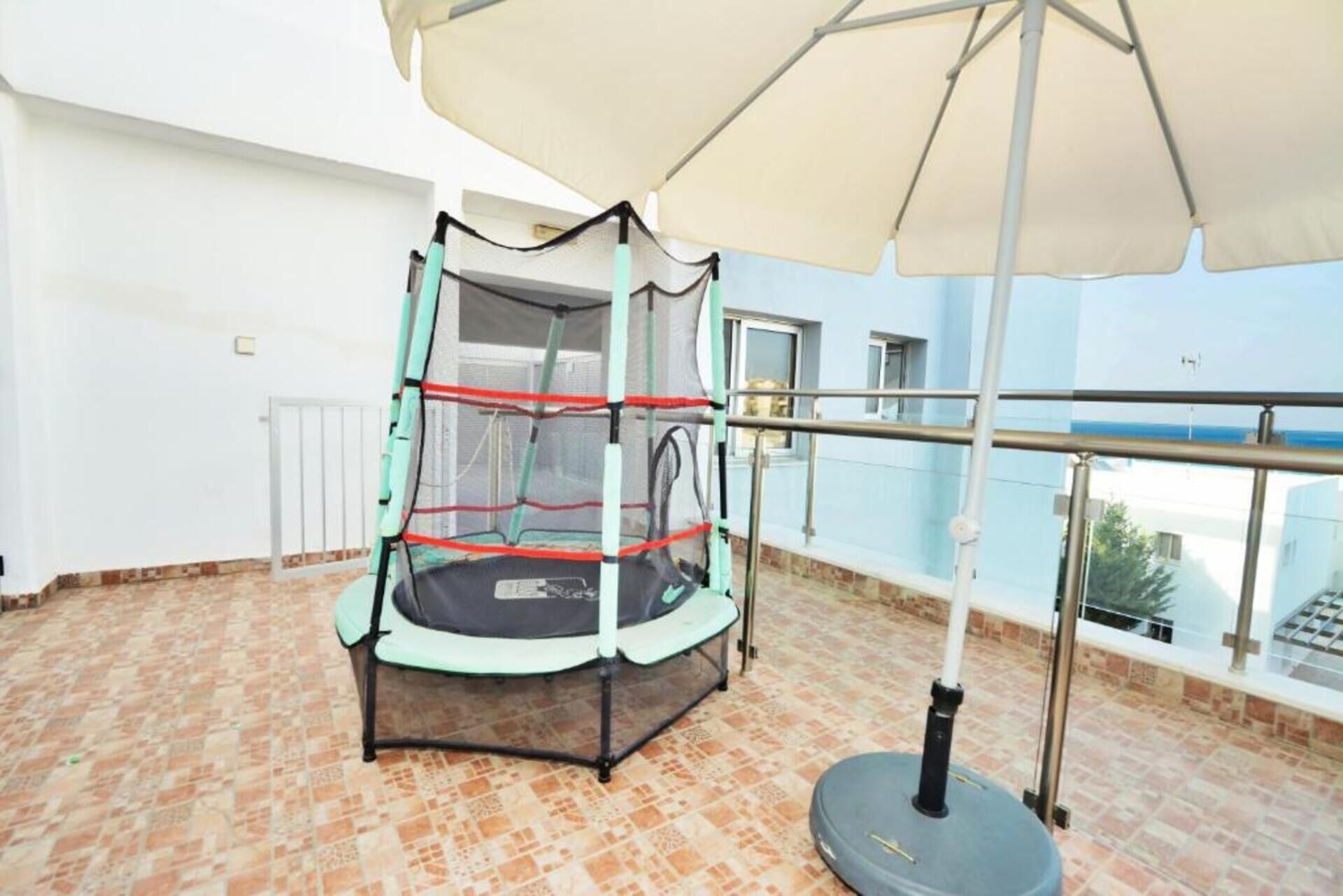 Ein Balkon mit Trampolin, Sicherheitsnetz, Sonnenschirm und Blick aufs Meer.