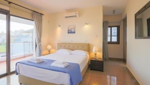 Quarto de hotel com uma cama grande, duas mesas de cabeceira com luminárias, um ar condicionado, uma janela com cortinas e vista para o exterior.