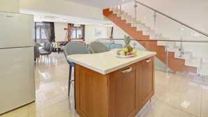 Cozinha moderna com ilha central, área de refeições com cadeiras e escada que leva a um andar superior.