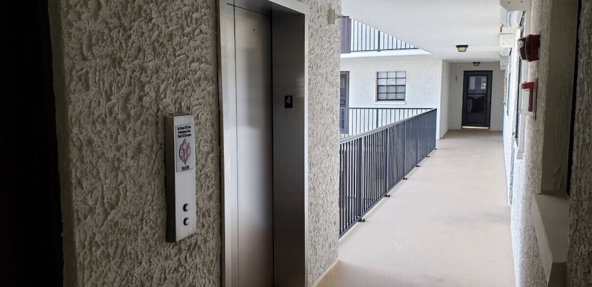 Corredor com parede texturizada, um elevador e um corrimão que leva a um andar superior.